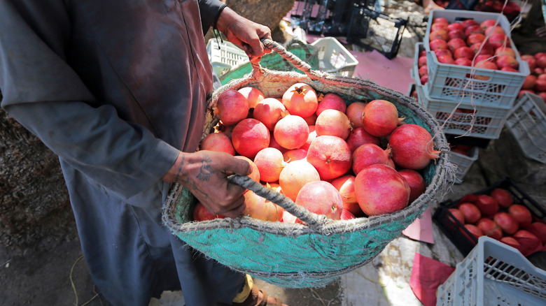 Person holding a basket of pomegranates at a local street market