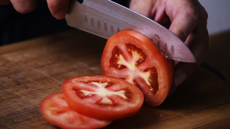 knife slicing tomatoes on board