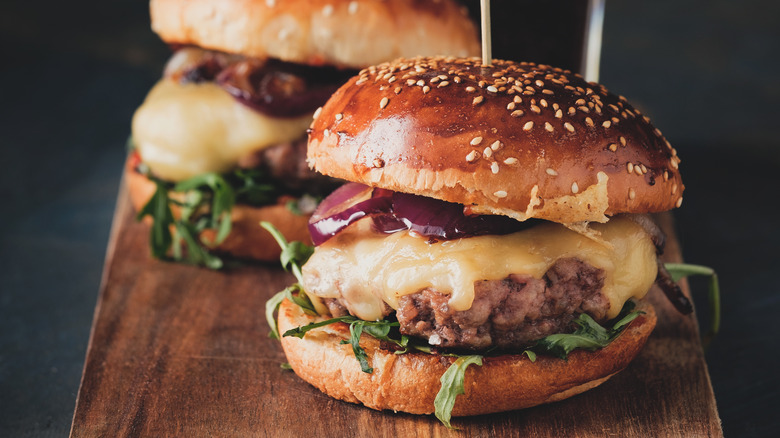 A burger with melted cheese on a wooden board