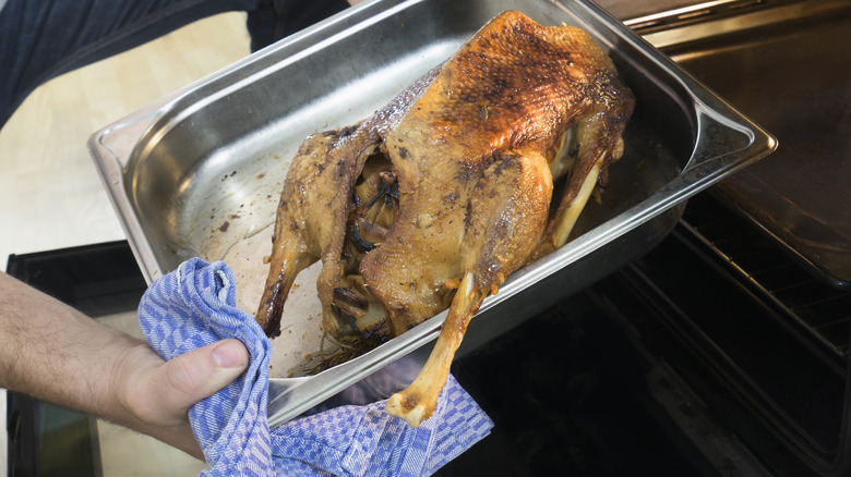 Chef removing chicken from oven with towel