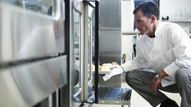 Chef removing bread from oven with towel