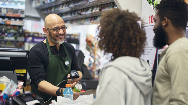 A couple purchasing groceries from a smiling clerk in a convenience store