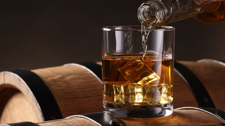 Pouring a whiskey on a barrel.