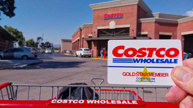 A person holding a Costco membership card in front of the store front