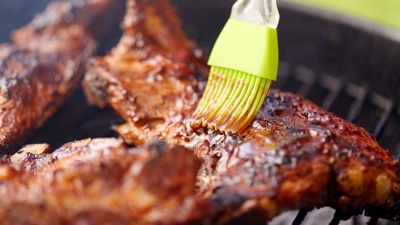 spreading barbecue sauce on meat with brush