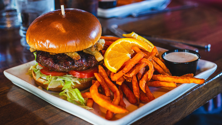 A burger is served and sweet potato fries on the side.