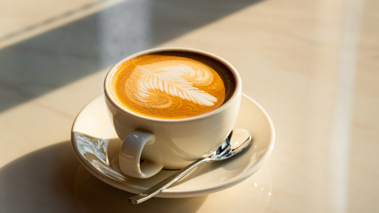 Latte with latte art in a white cup with a saucer and a spoon