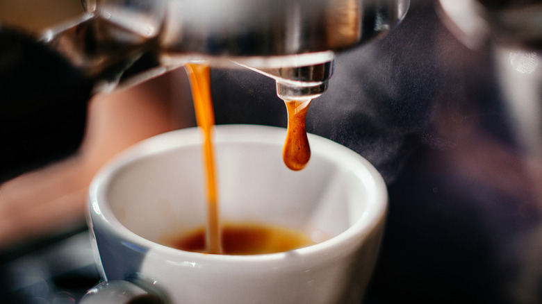 Espresso shot being pulled and into a small white espresso cup