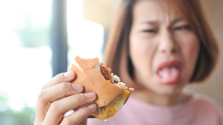 Woman making yucky face while holding half eaten burger