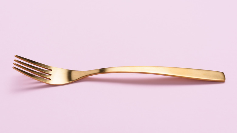 Golden fork on pink background