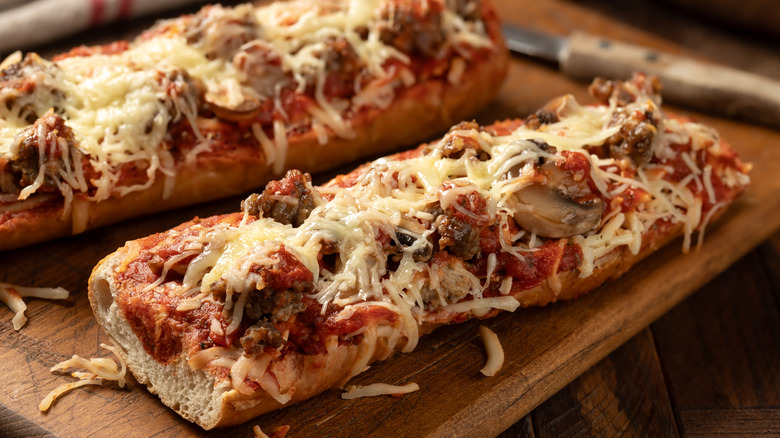 Two long French bread pizzas on a wooden cutting board