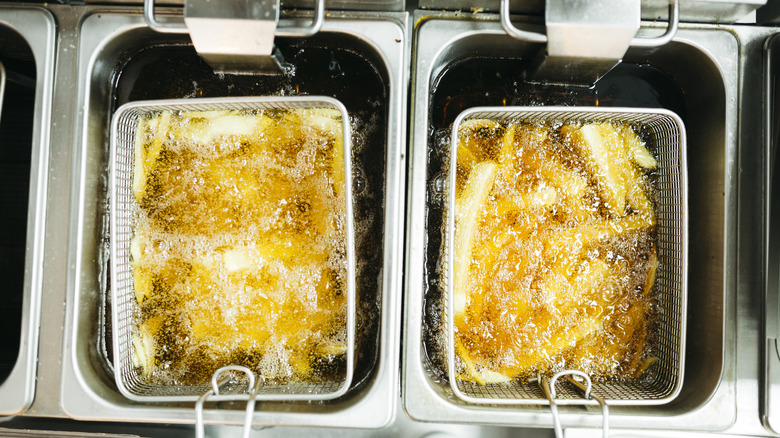 Two sets of fries cooking in oil in fryer baskets