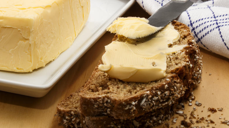 Thick butter being spread on wheat bread