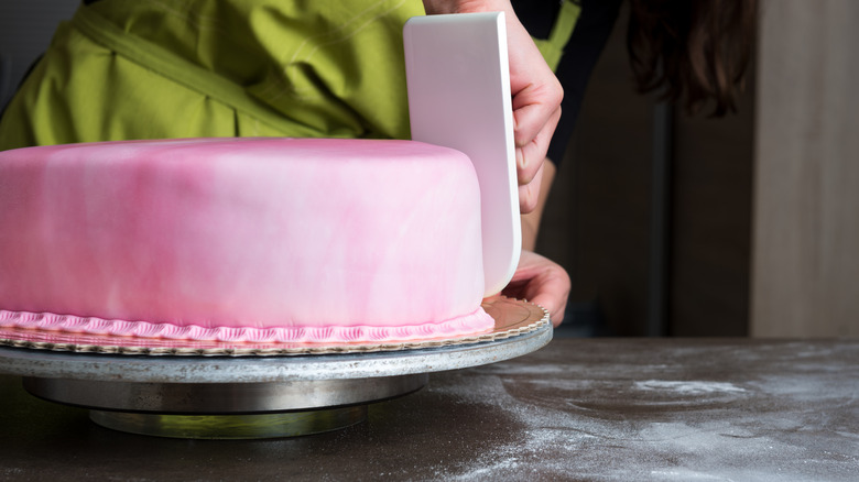 Spreading pink fondant on cake