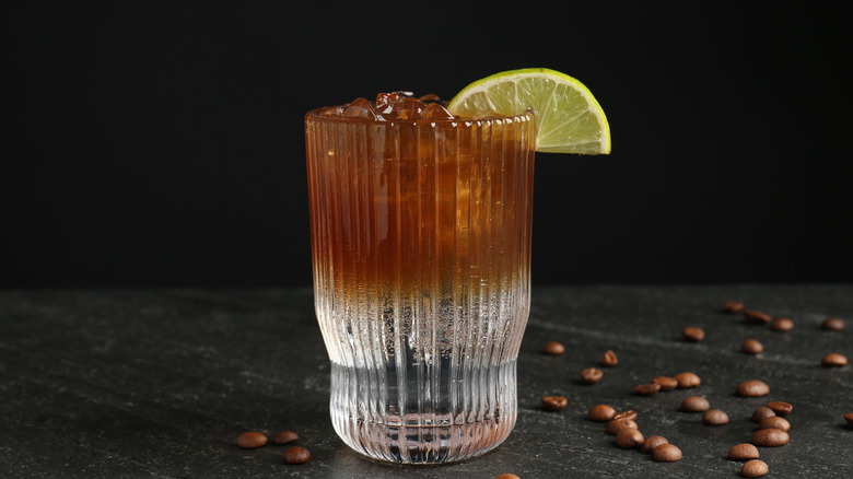 espresso tonic with a slice of lime and coffee beans scattered around