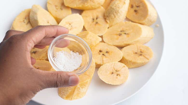 Hand holding salt over raw plantains 