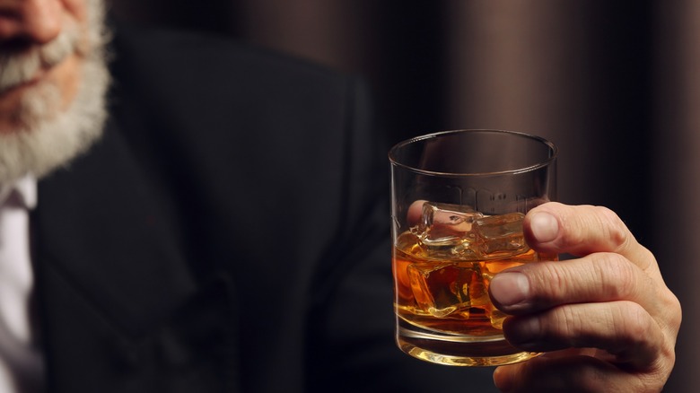 Gray-bearded man staring at a glass of bourbon