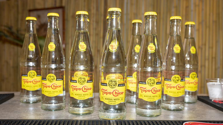 Several Topo Chico bottles lined up along a bar