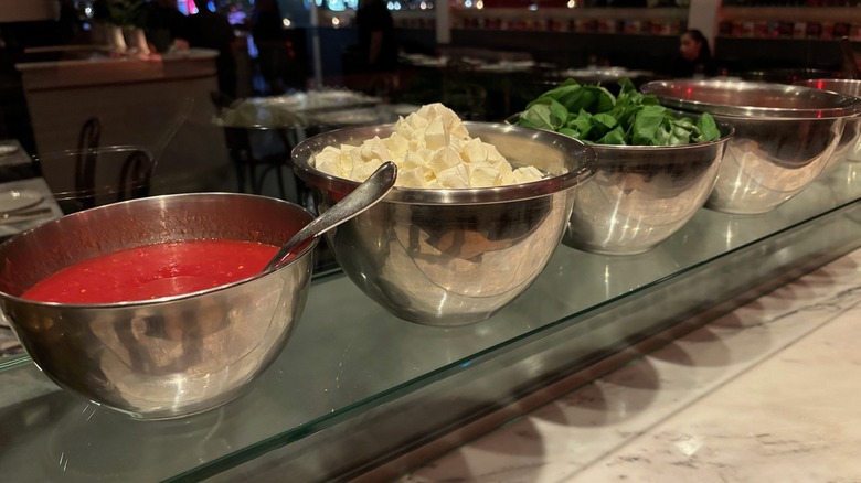 Bowls of pizza sauce, cheese, and basil