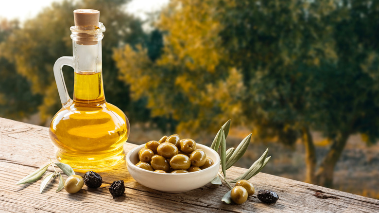 Glass bottle of olive oil and bowl of olives on wood table in olive grove