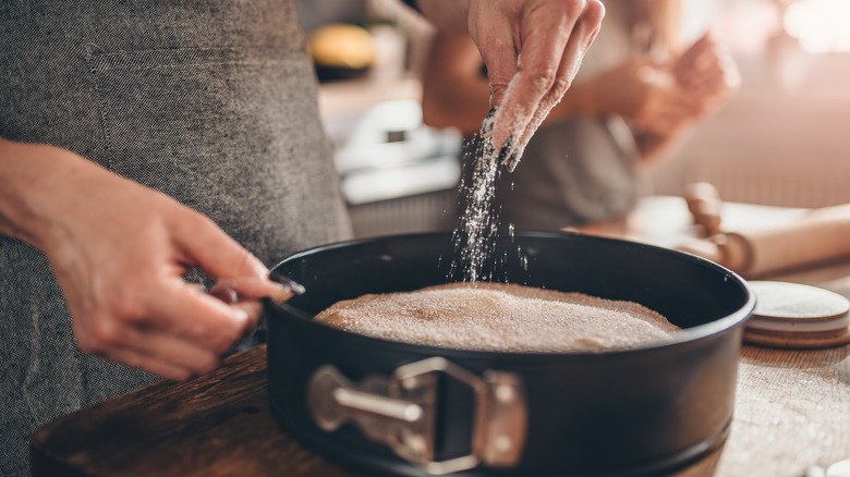 person sprinkling sugar into a cake pan