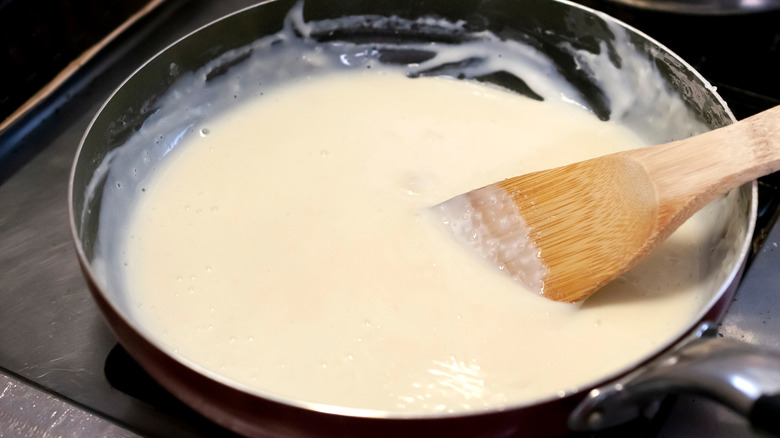 wooden spoon stirring white sauce in pan