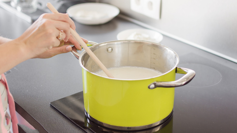 Person stirring white sauce in a saucepan