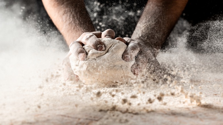 hands kneading dough on floured surface