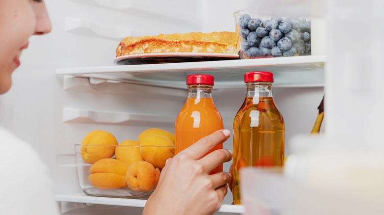woman placing juice glass bottle in fridge
