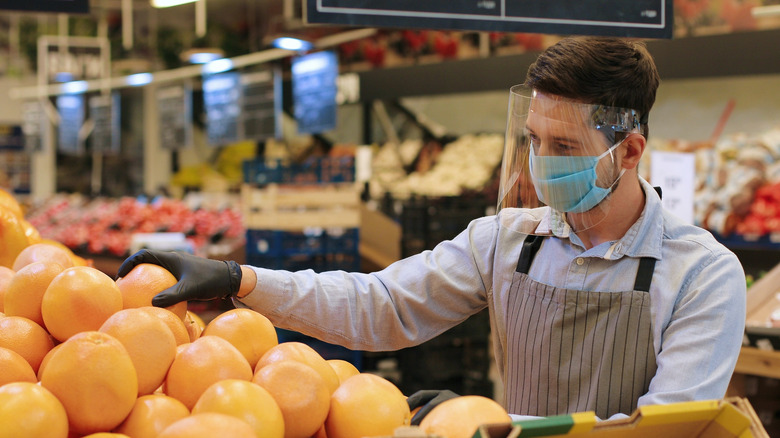 masked grocery employee stocking produce