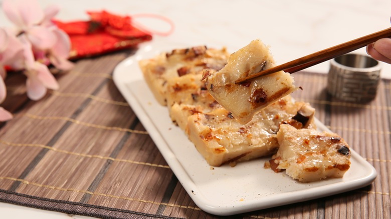 Person eating turnip cakes with chopsticks on Lunar New Year dinner table