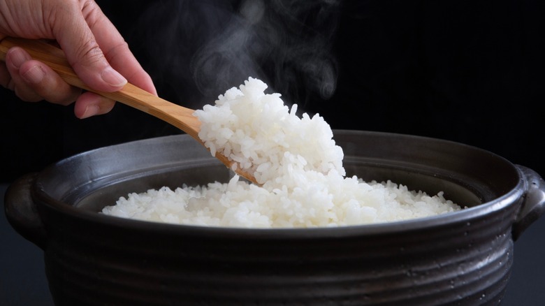 A hand scooping steaming white rice in a pot