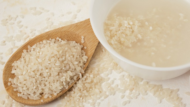 A scoop of dry white rice next to a bowl of rice white soaking in water