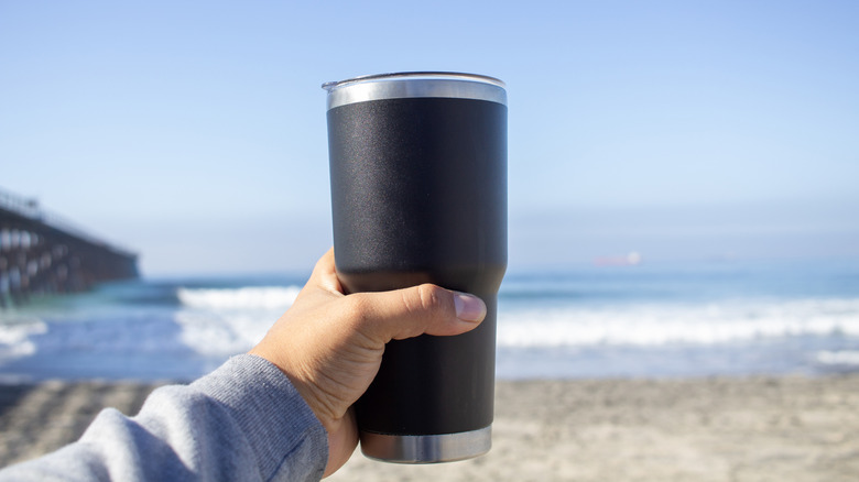 A traveler holds a travel mug on the beach