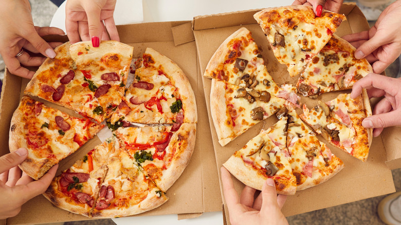 2 takeout pizzas with hands grabbing slices