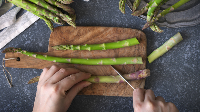 hands trimming asparagus over a wood cutting board