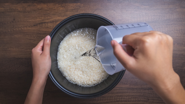 A hand pouring water out of a measuring cup into rice