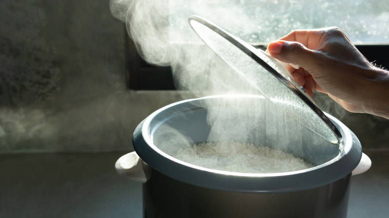 A hand lifting the lid of a rice pot