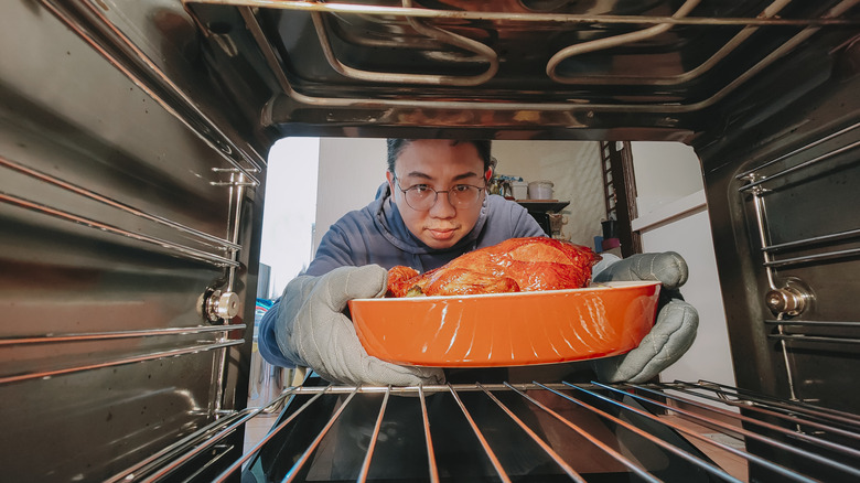 man taking chicken from oven