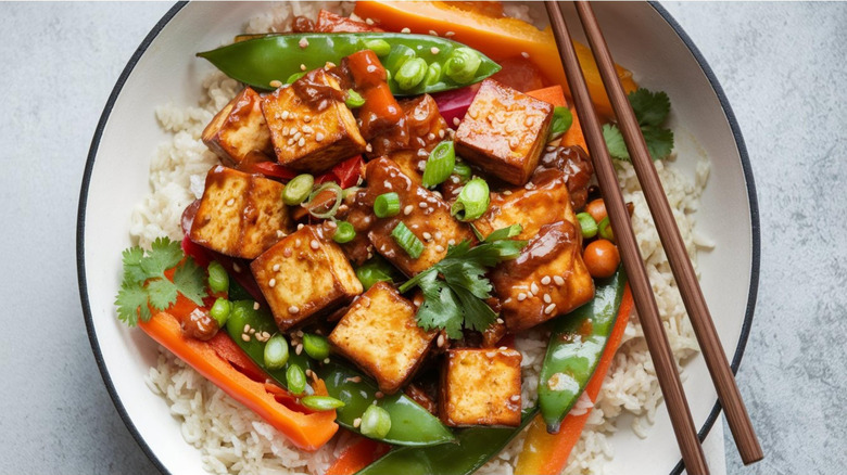 A stir fry with tofu, pea shoots, scallion, and bell peppers served over rice