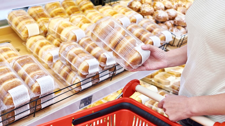 Shopper at a grocery store bakery picking up a pack of donuts