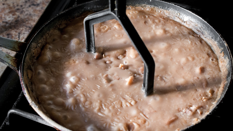 masher mashing beans in a saucepan on the stove