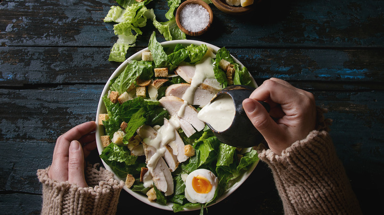 Hands pouring Caesar salad dressing