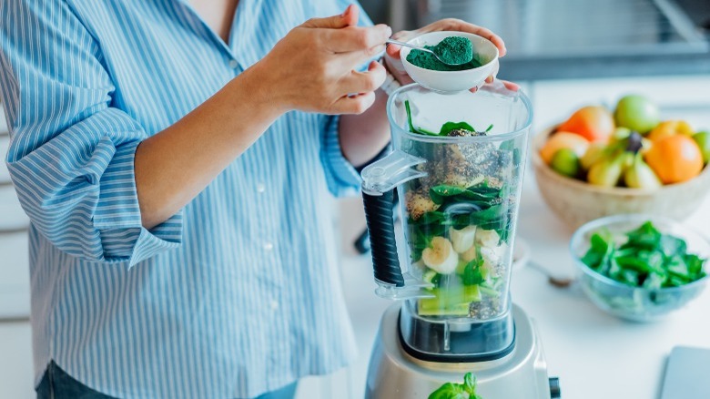 Woman adding spirulina to smoothie blender