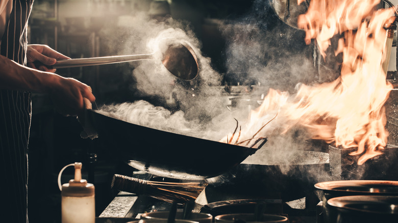 chef tossing wok with smoke and flames