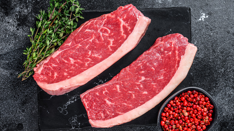 Two raw sirloin steaks on a board.