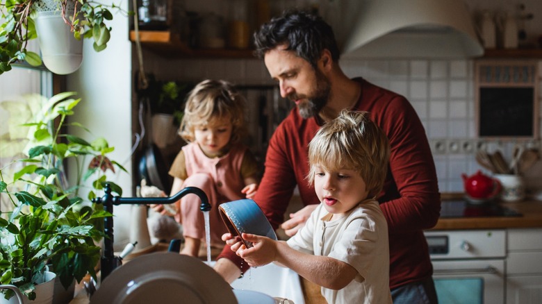 Man and two children cleaning stoneware in sink