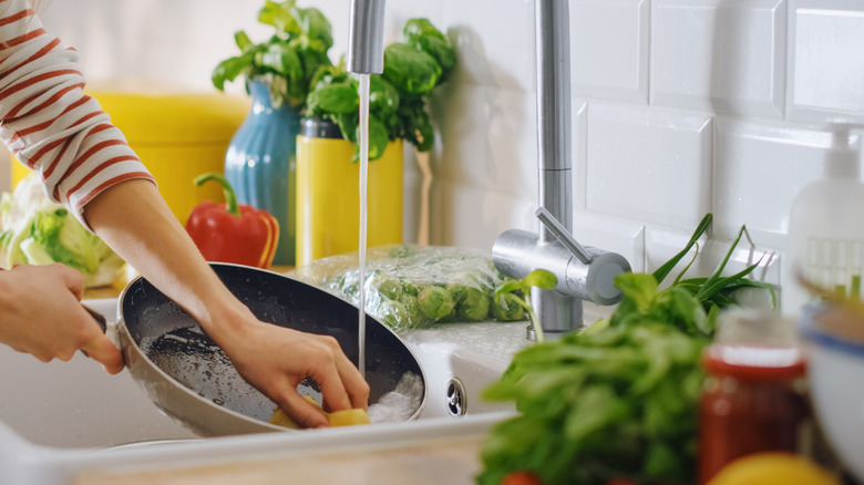 Hands washing pan in sink with sponge