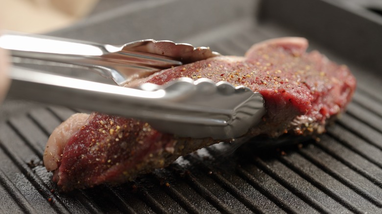 Tongs flipping steak on grill 