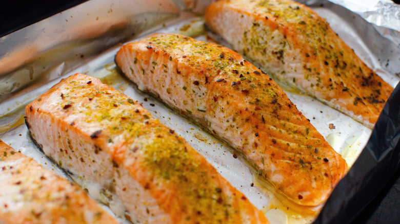 Baked fillets of seasoned salmon on a sheet of aluminum foil on a baking tray